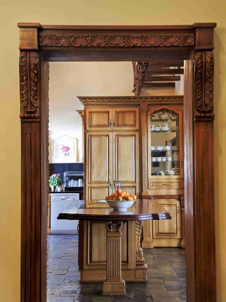 Carved timber doorway framing a view of kitchen cabinets and a central island