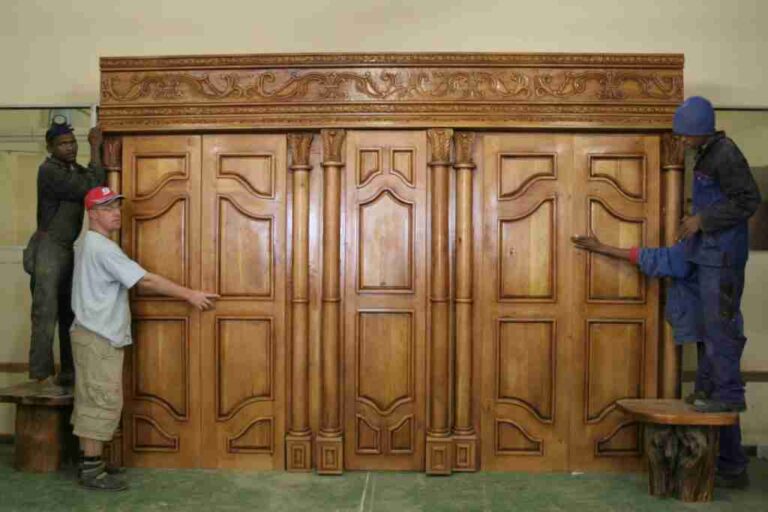 Large carved wardrobe with panelled doors and a decorative cornice, with people beside it