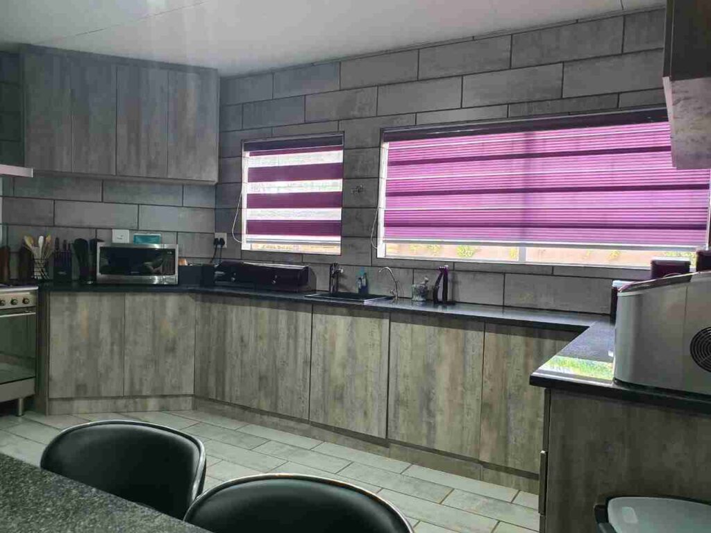 Grey fitted kitchen cabinets with a dark worktop below two windows