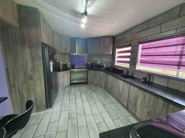 Narrow kitchen with grey fitted cabinets, dark worktops and windows along one side