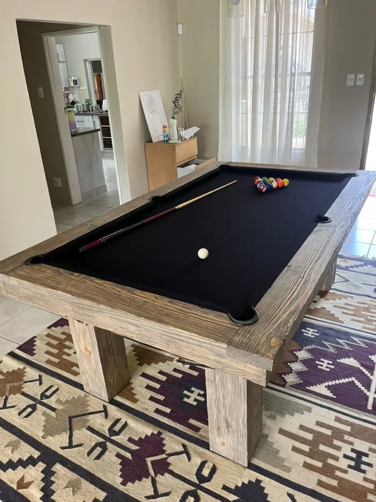 Wooden pool-dining table with its top removed, showing dark cloth and pool balls